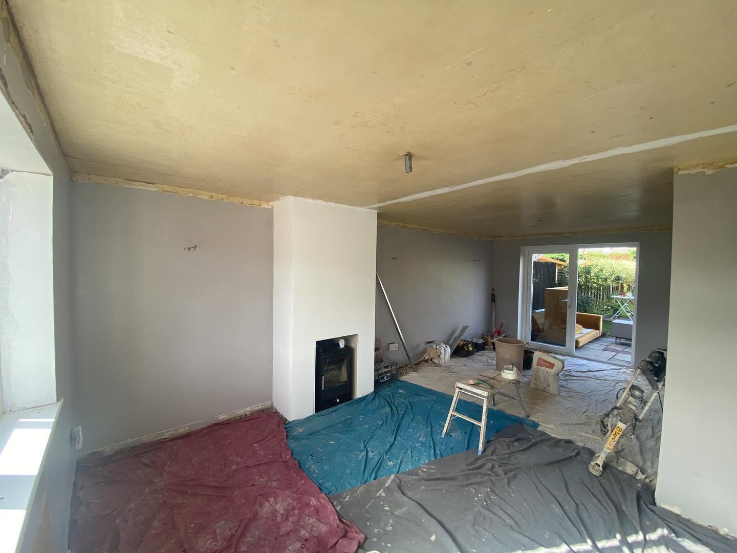 A living room with fresh plaster on the walls and ceiling, a stove in the white chimney breast