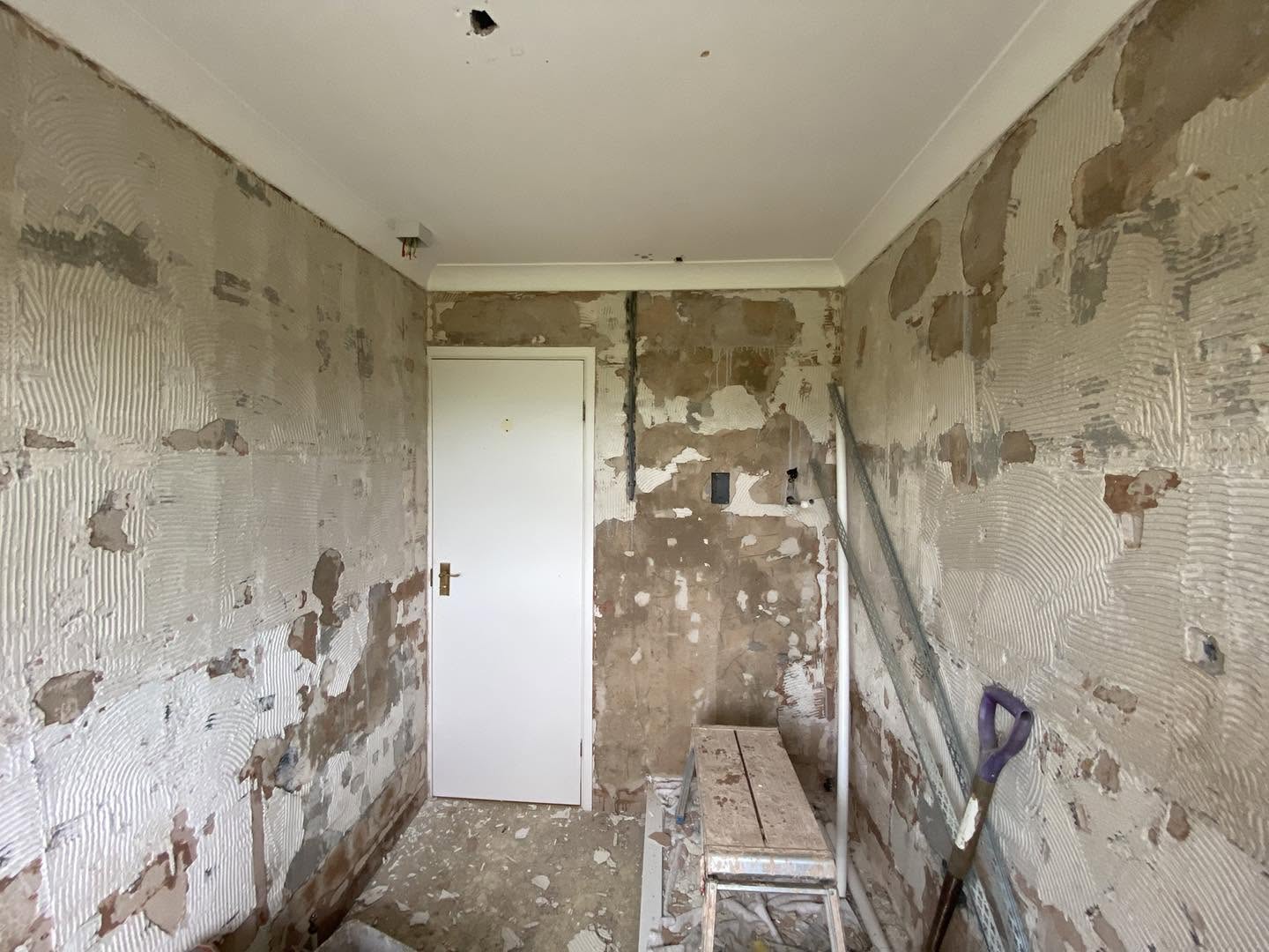 A small room with old tile adhesive and hacked-off walls, before plastering