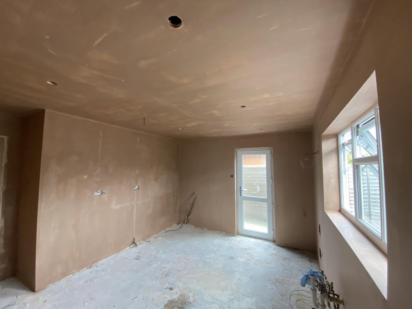 A room with fresh plaster walls and ceiling, a window and back door