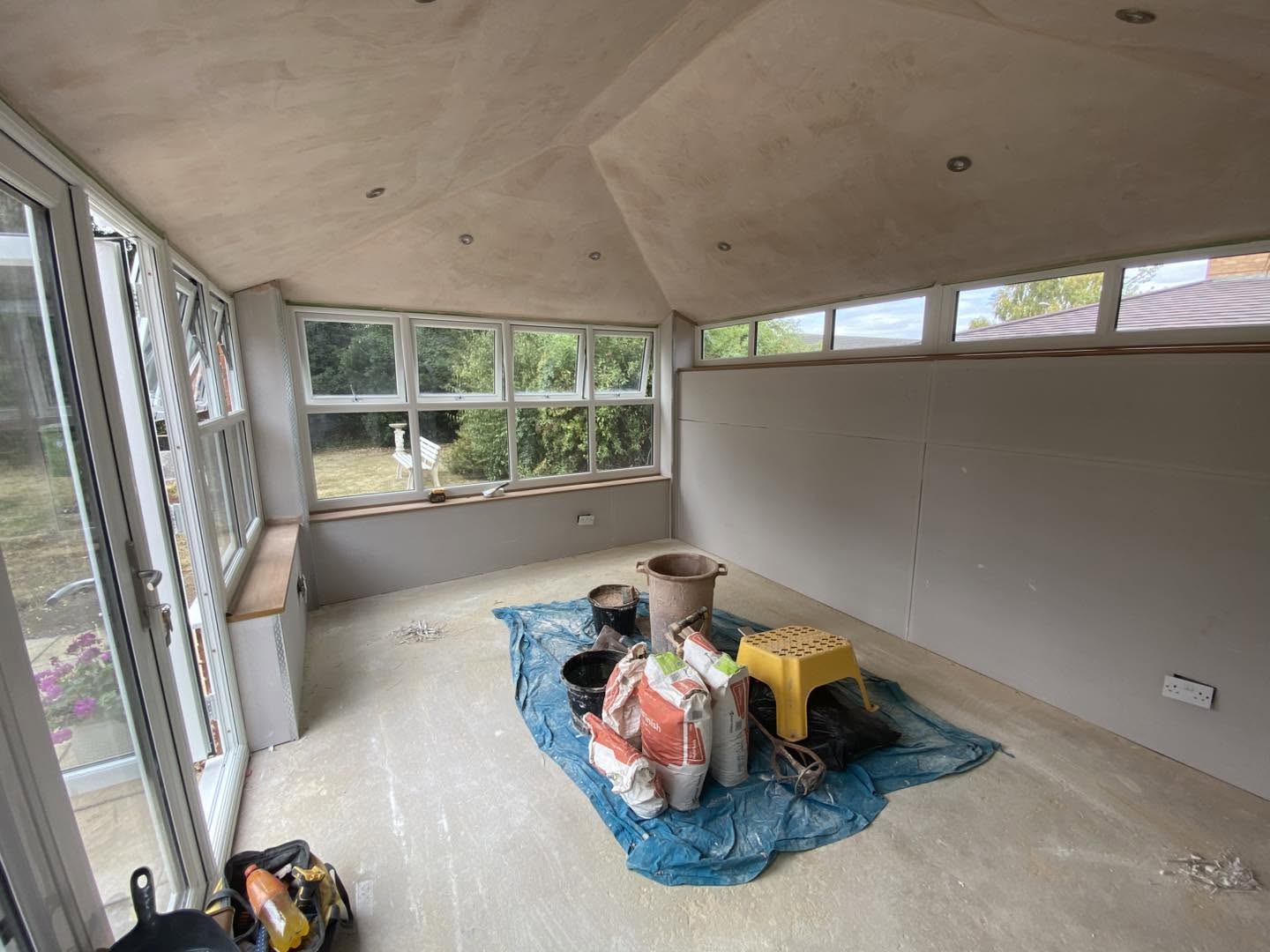 A garden room part way through, materials on a blue sheet under the new boarded ceiling