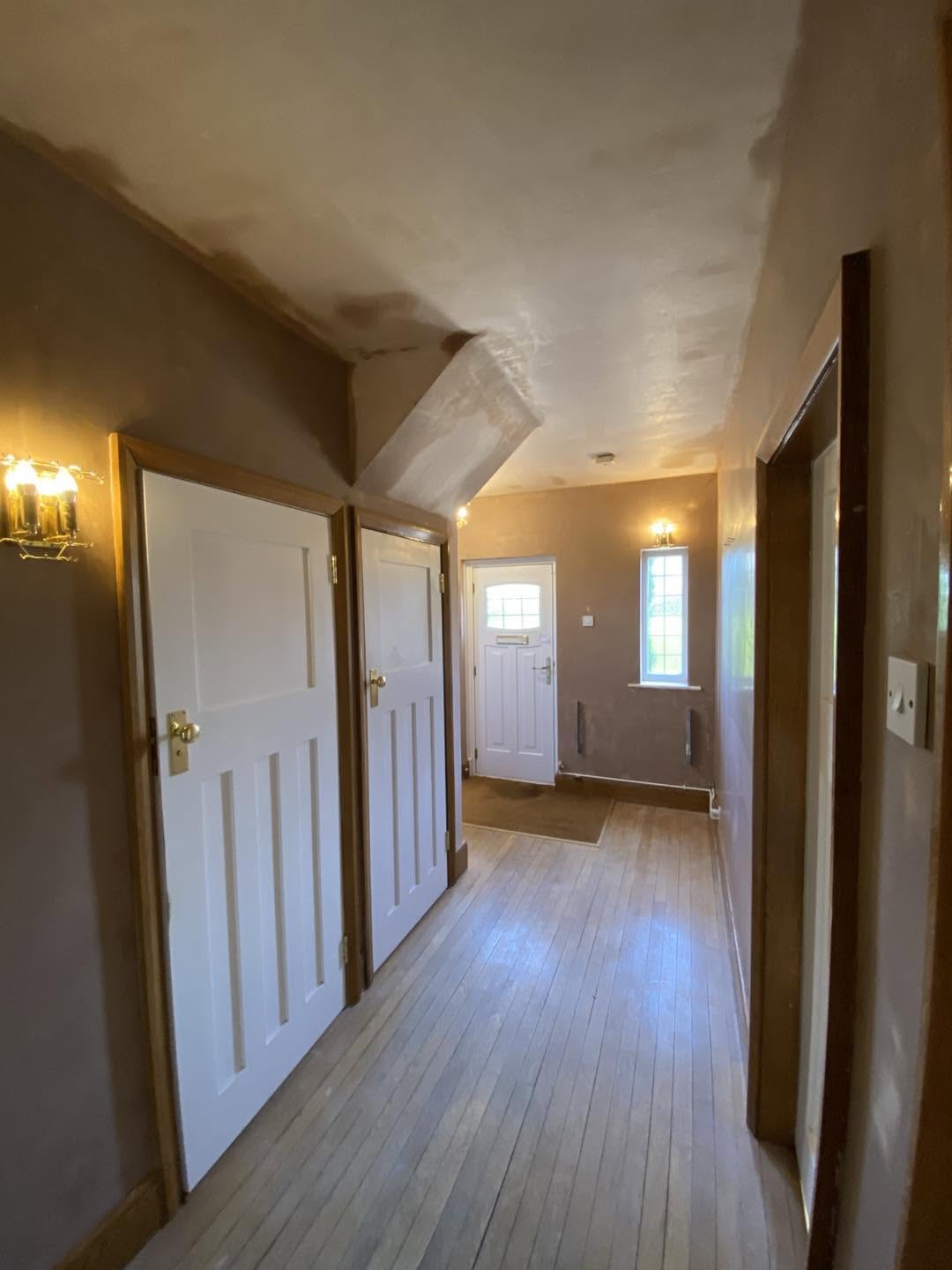 A long hallway with freshly plastered walls and ceiling, wall lights and panelled doors