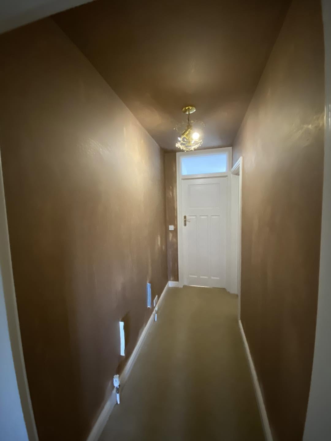 A long hallway in smooth fresh plaster, the front door at the far end
