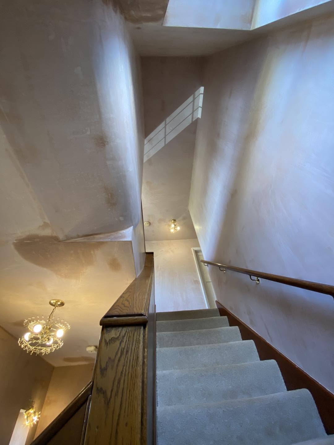 Looking down the stairwell, freshly plastered walls under a skylight