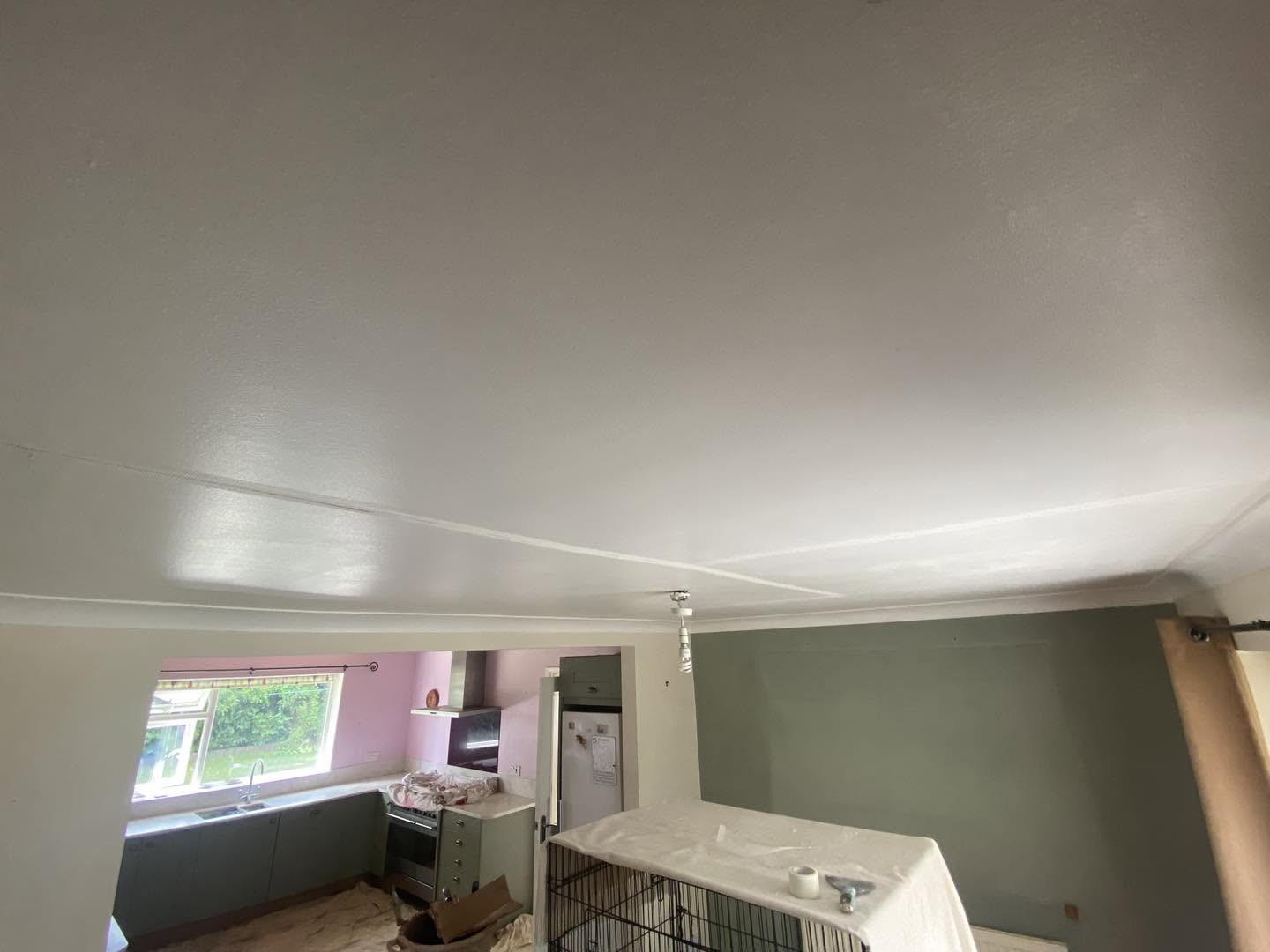 A ceiling freshly skimmed over a furnished room with pink and green walls