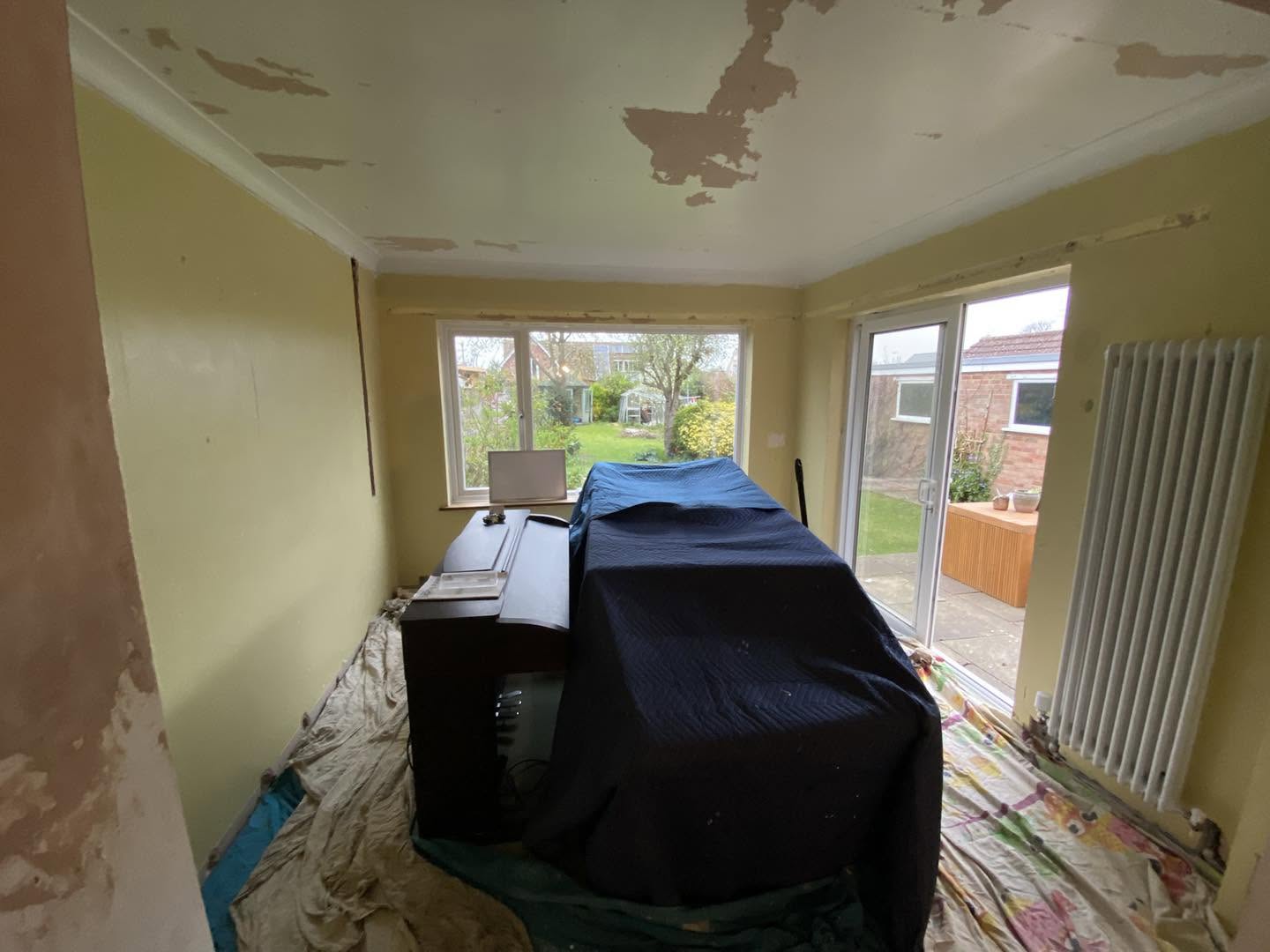 A living room with old yellow walls and a damaged ceiling, furniture covered
