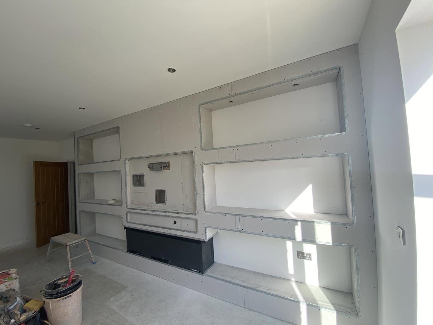 A plasterboard media wall with recessed shelves, finished in white