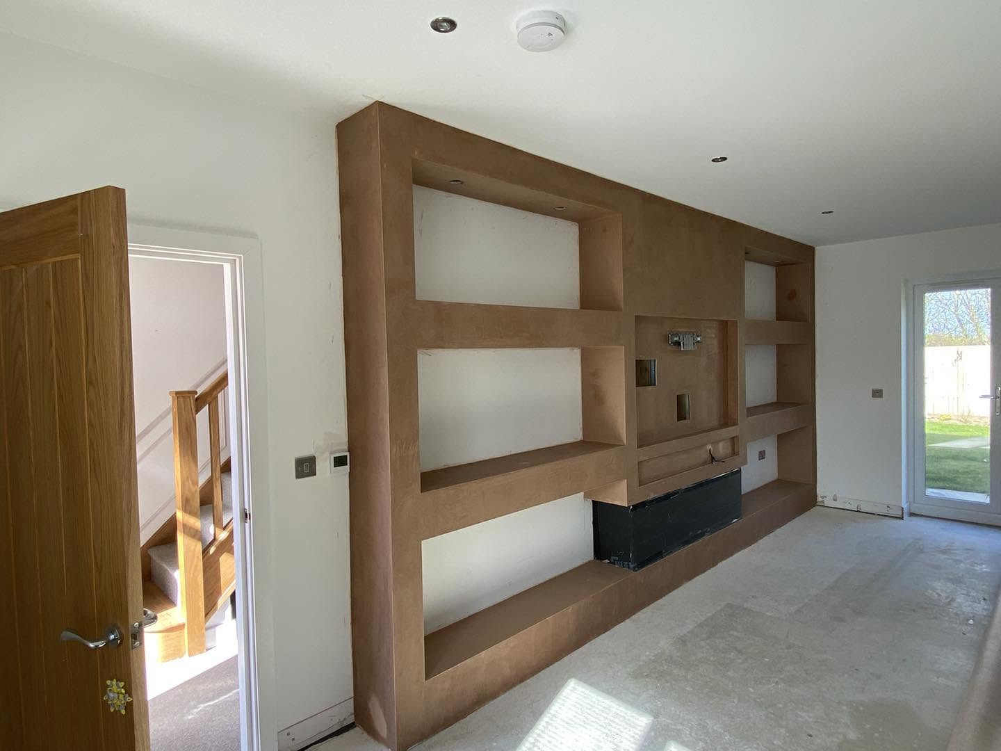 The media wall with its shelving freshly plastered, beside an oak door