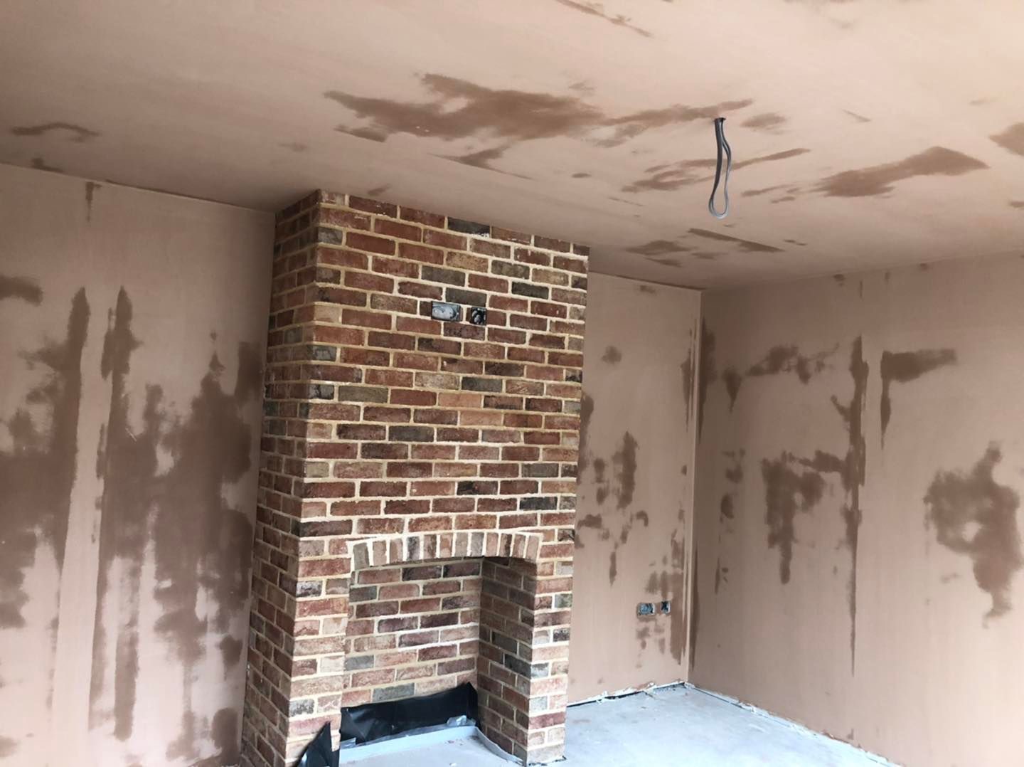 A room with freshly skimmed walls and ceiling still drying, an exposed brick chimney breast and fireplace opening