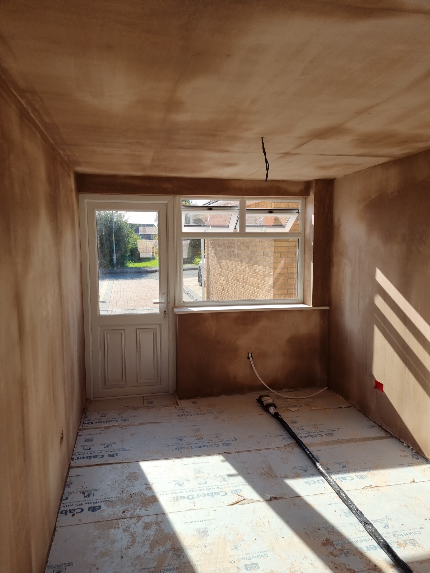 A garage conversion freshly plastered, white door and window at the end