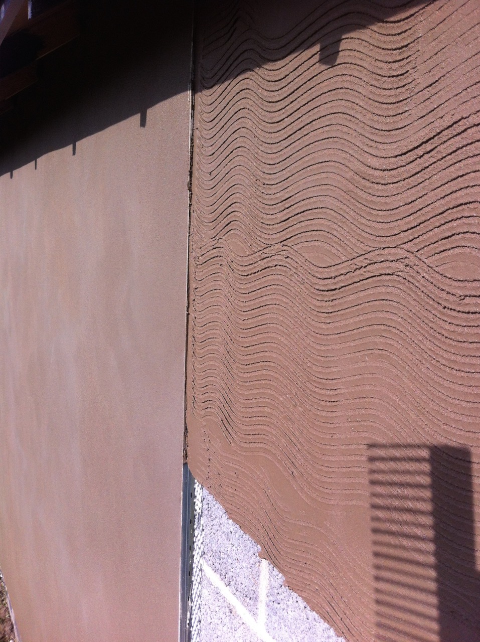A combed scratch coat beside finished render on blockwork