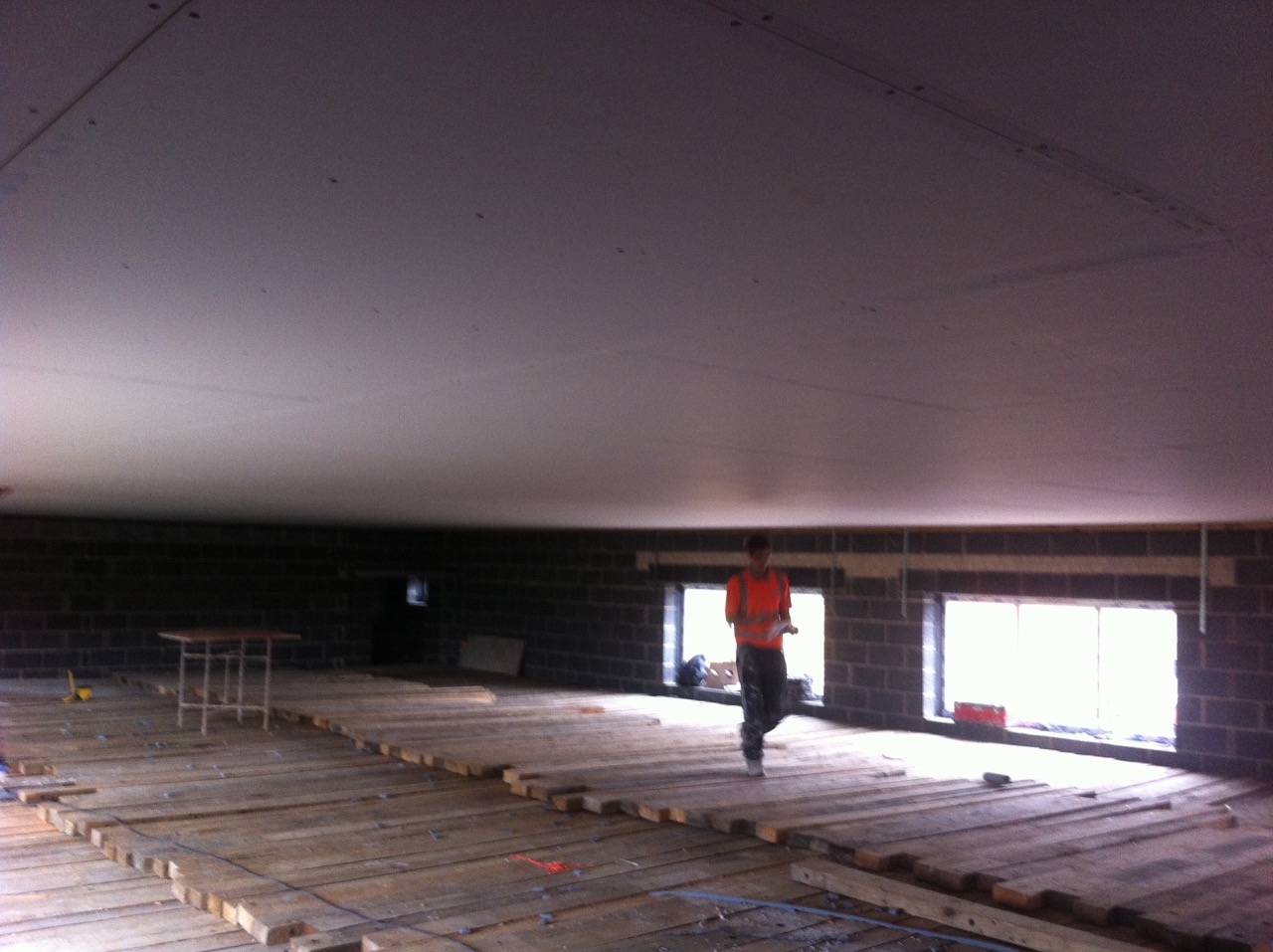 A large room with a boarded ceiling, a worker in orange hi-vis