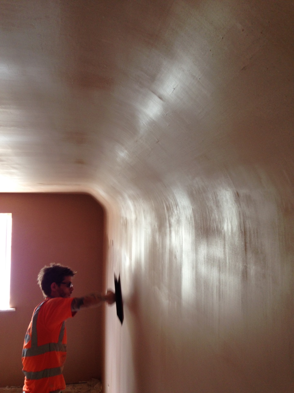 A plasterer in hi-vis skimming a wall with a trowel